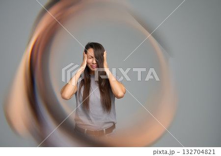 Woman holding head in pain surrounded by circular distortion symbolizing migraine or tinnitus Woman holding head in pain surrounded by circular distortion symbolizing migraine or tinnitus 132704821