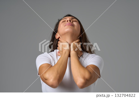 Woman holding neck in pain and looking up showing tension or discomfort in throat area indoors Woman holding neck in pain and looking up showing tension or discomfort in throat area indoors 132704822
