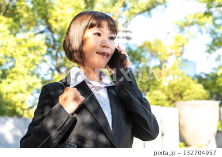 外出先で電話対応をするスーツの女性 外出先で電話対応をするスーツの女性 132704957