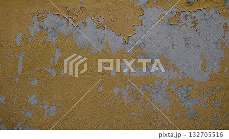 Close-up of an old concrete wall with yellow paint peeling and cracking, revealing faded grey plaster underneath. Weathered and aged surface ideal for use as grunge, urban decay 132705516