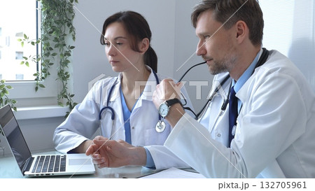 Two doctors are studying medical charts on a laptop, discussing patient data in a hospital or clinical setting. Medicine and healthcare concept. 132705961