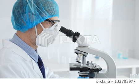 Experienced scientist examining microscopic sample, wearing full protective gear inside sterile research laboratory. Health care and science concept Experienced scientist examining microscopic sample, wearing full protective gear inside sterile research laboratory. Health care and science concept 132705977