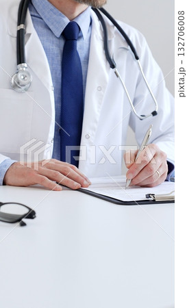 Unreckognisable doctor man writing a prescription and filling out medical records on a clipboard in an office setting. Medicine and health care concept 132706008