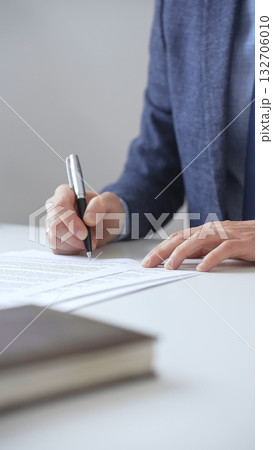 Closeup of businessman signing a contract with elegant pen, wearing a blue suit and a wristwatch, sitting at a white desk in office. Business people concept 132706010
