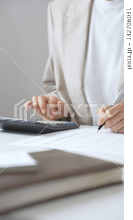 Businesswoman is calculating annual tax using calculator and taking notes in the office, managing domestic budget and checking financial documents. Audit and taxes in business 132706031