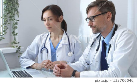 Two doctors are examining medical records on a laptop, engaging in a focused discussion about patient data within a hospital or clinical setting. Medicine and health care concept Two doctors are examining medical records on a laptop, engaging in a focused discussion about patient data within a hospital or clinical setting. Medicine and health care concept 132706046