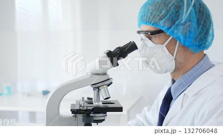 Experienced scientist examining microscopic sample, wearing full protective gear inside sterile research laboratory. Health care and science concept 132706048