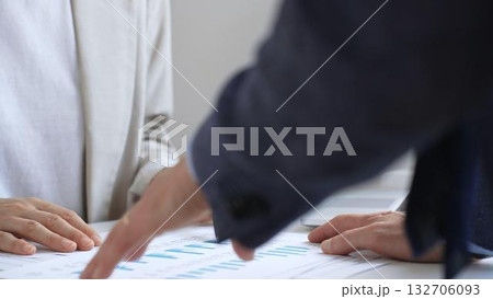 Financial analysts reviewing laptop screen and printed documents, pointing at data charts and discussing investment strategies together in modern office setting. Business people concept 132706093