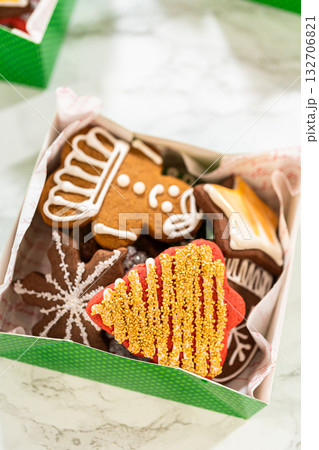 Captured from a close-up perspective, green holiday gift boxes filled with decorated Christmas cookies are neatly arranged with parchment lining. The festive assortment includes mitten, tree, and star Captured from a close-up perspective, green holiday gift boxes filled with decorated Christmas cookies are neatly arranged with parchment lining. The festive assortment includes mitten, tree, and star 132706821