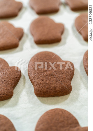 Front-facing view of freshly baked Pale Gingerbread Cookies in mitten shapes resting on a parchment-lined tray, just out of the oven. 132706822