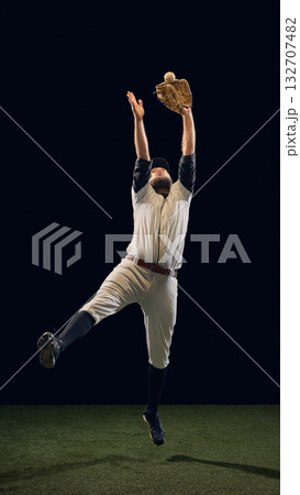 Baseball player jumping with glove raised to catch ball on dark background. Baseball player jumping with glove raised to catch ball on dark background. 132707482