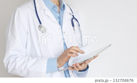 Unknown female doctor, wearing white coat over a blue blouse and a stethoscope, is using a digital tablet, suggesting innovative healthcare practices in medicine. Health care and medicine concept 132708676