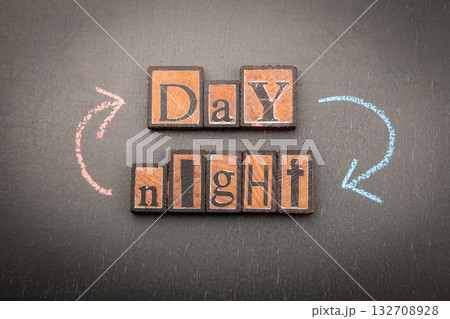 Wooden blocks spelling Day and Night with chalk arrows on dark background, symbolizing time, balance 132708928