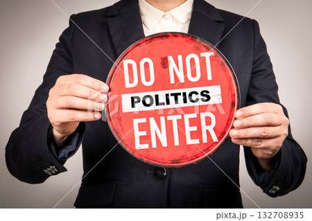 Person in suit holding a red round sign with the words do not enter POLITICS. Symbolizing 132708935