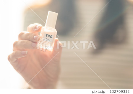 Woman holding a bottle of TPO free gel polish in bright natural light. Safe manicure product without Trimethylbenzoyl Diphenylphosphine Oxide for health-conscious consumers. 132709332