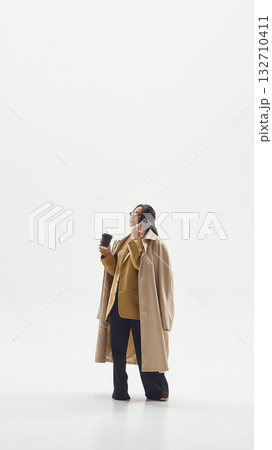 Modern businesswoman in beige coat multitasking with phone and coffee representing leadership and focus Modern businesswoman in beige coat multitasking with phone and coffee representing leadership and focus 132710411