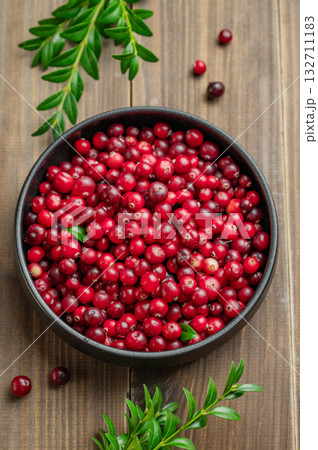 layout of fresh cranberries in a dark bowl on a wooden background with green branch. 132711183