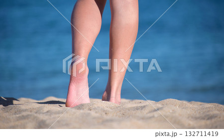 Close up of female feet walking barefoot on white grainy sand of golden beach on blue ocean water background Close up of female feet walking barefoot on white grainy sand of golden beach on blue ocean water background 132711419