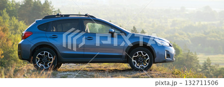 Blue off road car at dawn on grassy hill on distant foggy city landscape background. Extreme travel on a SUV automobile Blue off road car at dawn on grassy hill on distant foggy city landscape background. Extreme travel on a SUV automobile 132711506