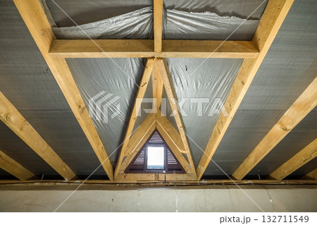 Attic of a building with wooden beams of a roof structure and a small window. 132711549
