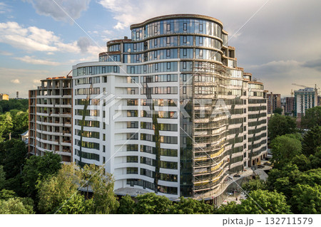 Apartment or office tall building under construction. Brick walls, glass windows, scaffolding and concrete support pillars Apartment or office tall building under construction. Brick walls, glass windows, scaffolding and concrete support pillars 132711579