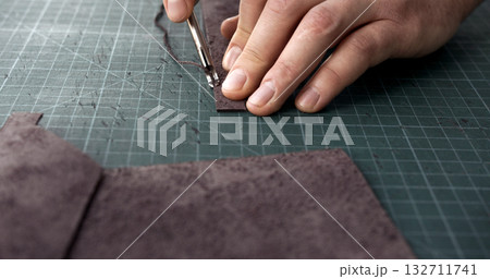 Craftsman using edge tool on leather strip for handmade leather goods production 132711741