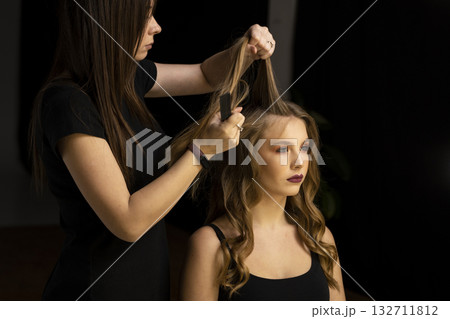 Hairstylist styling long wavy hair of young woman with comb in beauty studio 132711812