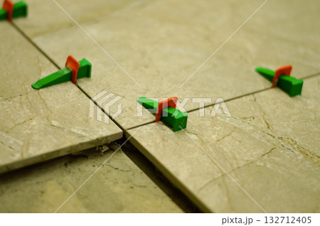 The installer is using a modern lash tile leveling method, which involves placing special clips and wedges to align the tiles perfectly on the wall before the adhesive dries. 132712405