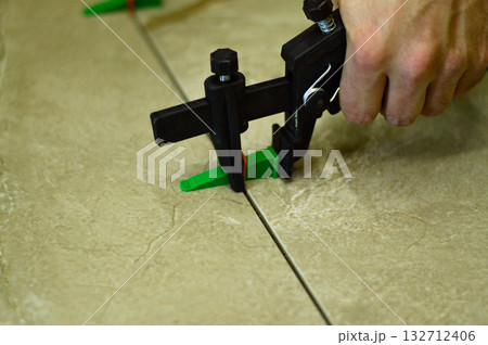 Using a specialized lash leveling system, the installer ensures each ceramic tile is perfectly aligned and flush with its neighbors on the adhesive-coated wall. Using a specialized lash leveling system, the installer ensures each ceramic tile is perfectly aligned and flush with its neighbors on the adhesive-coated wall. 132712406