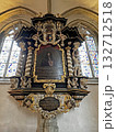A richly decorated painted memorial in Osnabruk cathedral, featuring gold and white ornamentation, Latin script, angel figures, and stained glass windows behind. 132712518
