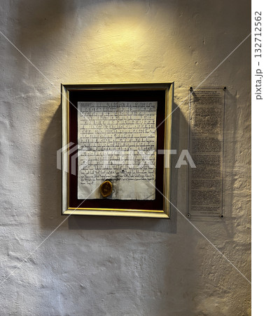 An illuminated framed medieval document with seal hangs on a textured wall in Osnabruk, supported by a modern explanation panel. 132712562