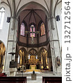 The spacious interior of Osnabruk cathedral reveals soaring gothic arches, tall windows with stained glass, a crucifix, and an ornately gilded altar. 132712564