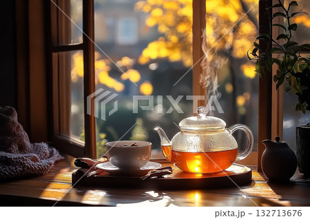 Teapot with steam coming out of it sits on a table next to a cup Teapot with steam coming out of it sits on a table next to a cup 132713676