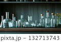 Row of glass vases and bottles are lined up on a wooden shelf 132713743