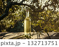 Bottle of olive oil sits on a wooden table next to a leafy tree 132713751