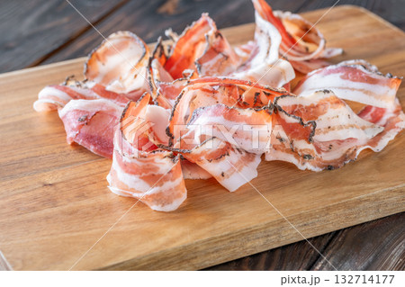 Rustic presentation of sliced Italian pancetta arranged neatly on wooden cutting board 132714177