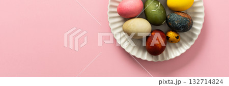 A variety of decorated Easter eggs are arranged on a circular plate against a soft pink background, showcasing vibrant colors and intricate designs for a seasonal celebration, banner 132714824