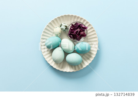 A plate holds several blue-painted Easter eggs and a couple of small patterned eggs, creating a festive atmosphere for the holiday celebration, small bowl of red cabbage, how to dye eggs blue A plate holds several blue-painted Easter eggs and a couple of small patterned eggs, creating a festive atmosphere for the holiday celebration, small bowl of red cabbage, how to dye eggs blue 132714839