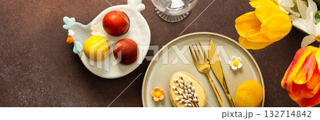 A beautifully arranged Easter table setting showcases a yellow napkin wrapped around a red apple, surrounded by vibrant flowers and a festive bunny decoration, banner A beautifully arranged Easter table setting showcases a yellow napkin wrapped around a red apple, surrounded by vibrant flowers and a festive bunny decoration, banner 132714842