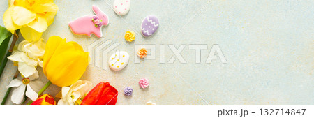 Bright tulips and daffodils surround playful Easter cookies and candies, showcasing the vibrant spirit of springtime festivities and holiday celebrations, banner 132714847