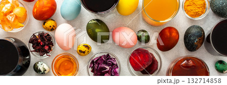 Colorful Easter eggs surround various bowls filled with natural dyes such as beets, turmeric and flower extracts hibiscus, red cabbage and onion peel, showcasing a creative egg decorating process 132714858