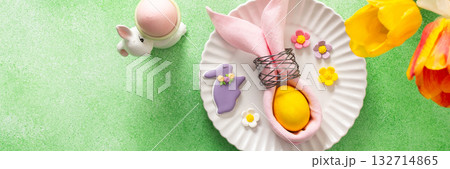 A beautifully arranged Easter table setting showcases a decorative egg nestled in a pink napkin, surrounded by a glass of water and fresh flowers, perfect for holiday gatherings, banner 132714865