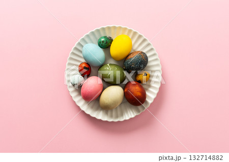 A collection of vibrant Easter eggs in various colors is artfully arranged on a white plate, set against a soft pink background, capturing the essence of the holiday's decorations A collection of vibrant Easter eggs in various colors is artfully arranged on a white plate, set against a soft pink background, capturing the essence of the holiday's decorations 132714882