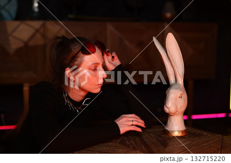 woman inspects rabbit head art at night, woman gazes at rabbit jewelry under dim red lighting 132715220