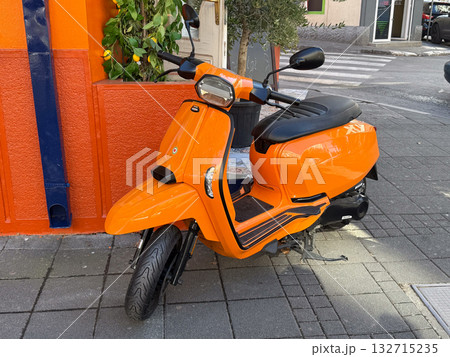 Bright orange scooter parked near colorful wall. Urban mobility, city lifestyle and cheerful street design. 132715235