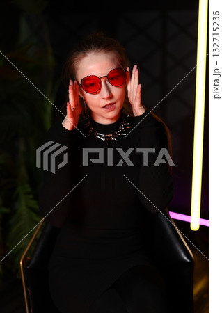woman in studio, dark studio scene featuring woman with red sunglasses and introspective expression 132715236