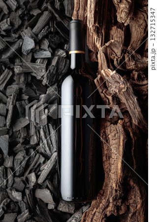 Bottle of red wine against a backdrop of charcoal and dry snags. 132715347