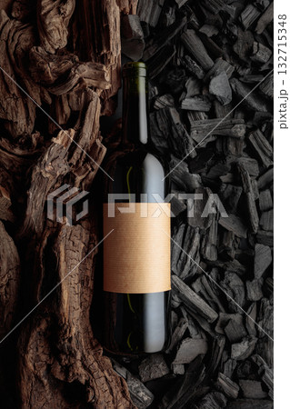 Bottle of red wine against a backdrop of charcoal and dry snags. 132715348