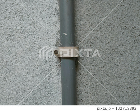 The image shows a PVC pipe with a pipe clip or saddle clamp. This type of clamp is used to secure the pipe to a wall or other surface. 132715892