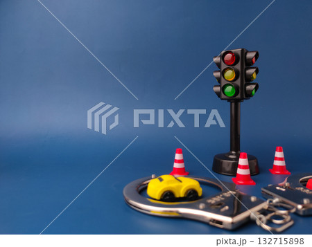 The image shows a miniature traffic light, a toy car, a pair of handcuffs, and several traffic cones on a blue background. The image shows a miniature traffic light, a toy car, a pair of handcuffs, and several traffic cones on a blue background. 132715898